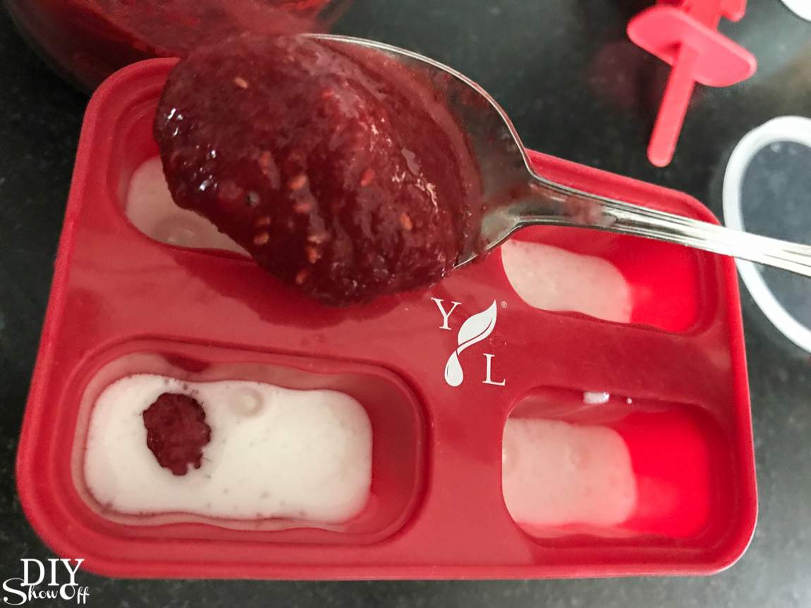 Spoon adding raspberry mixture into a popsicle mold during DIY popsicle preparation