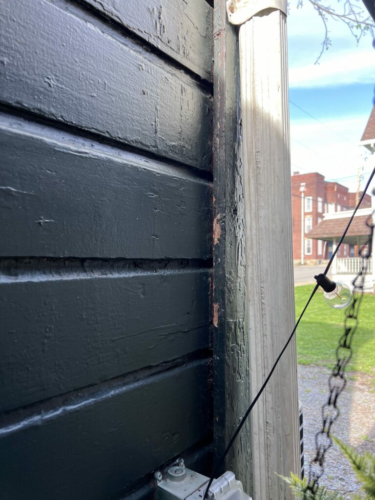 Scratches and paw prints on siding beside a white drainpipe from raccoon climbing